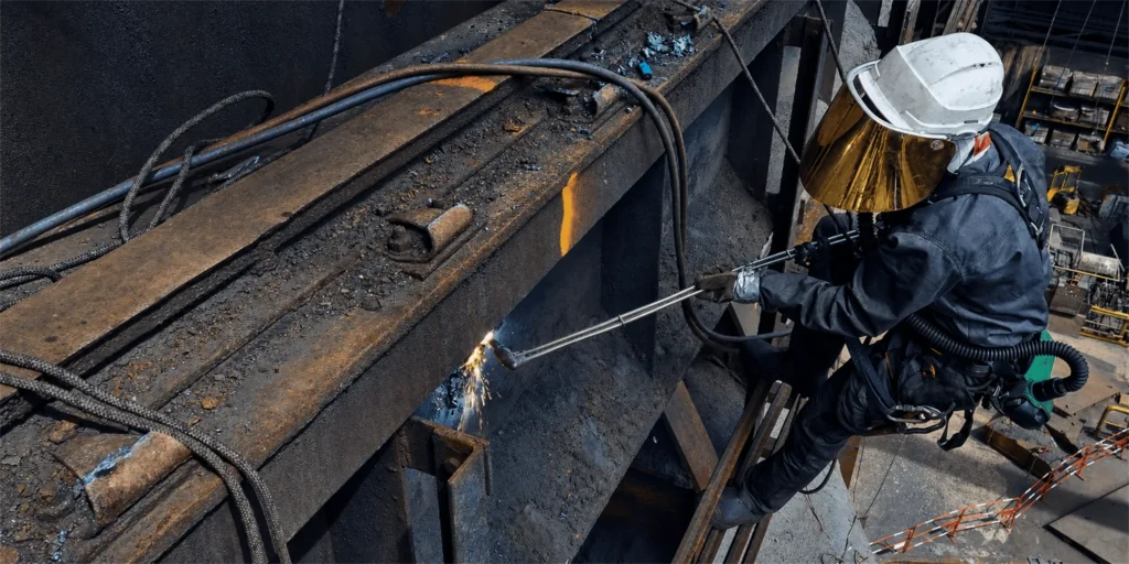 Cordiste réalisant une découpe au chalumeau sur une structure métallique industrielle